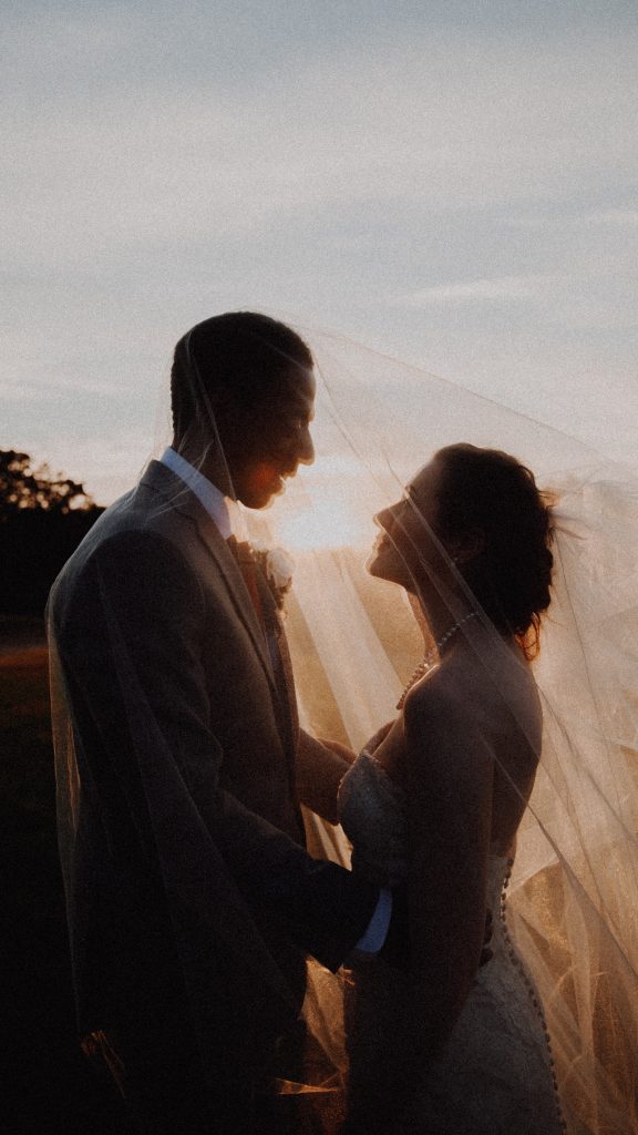 a photo of a bride and groom under a veil at sunset