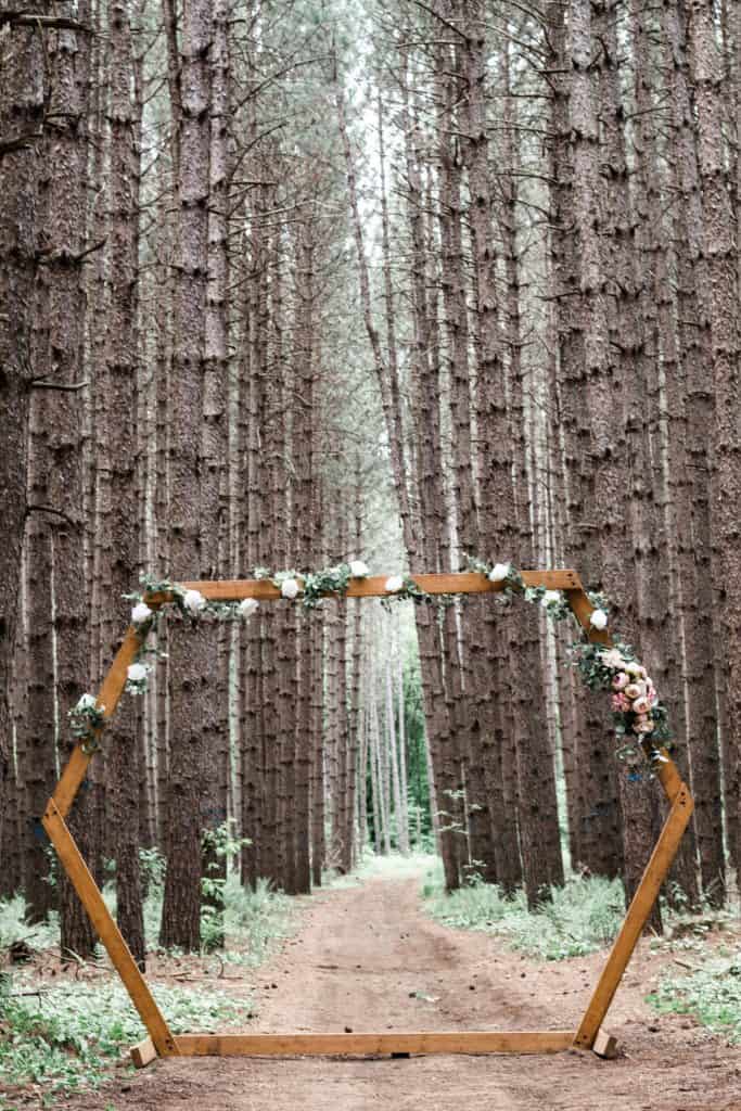 a hexagon wedding arch with floral accents in the woods