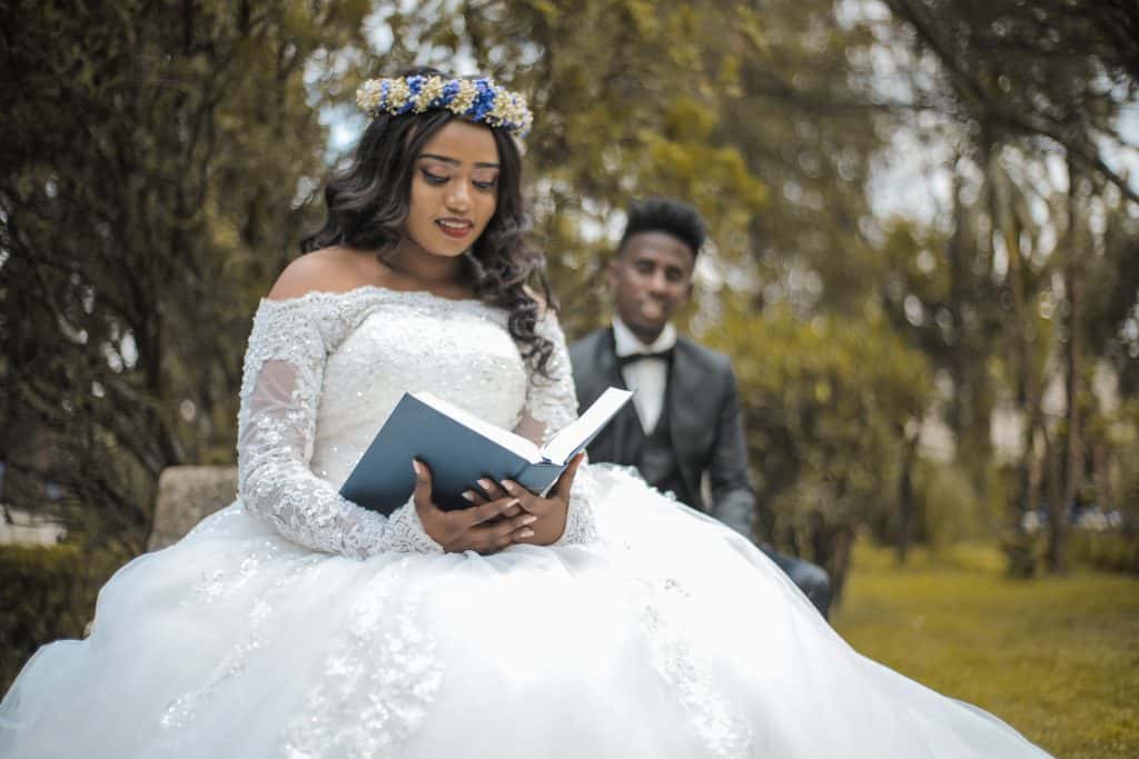 a bride reading a book with the groom behind her
