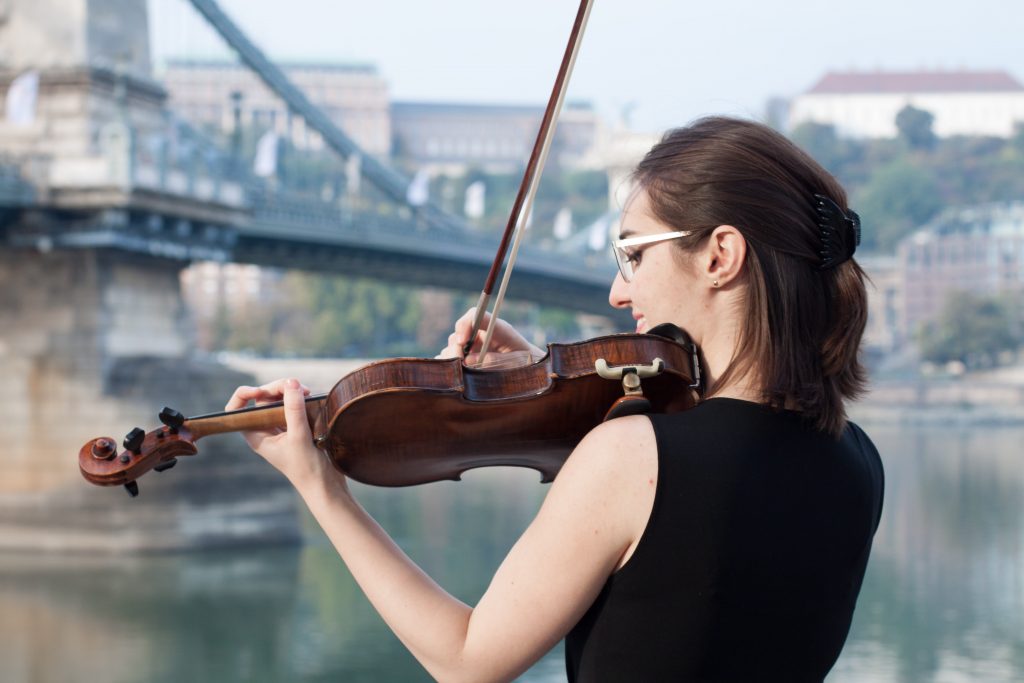 woman playing a violin overlooking a bridge