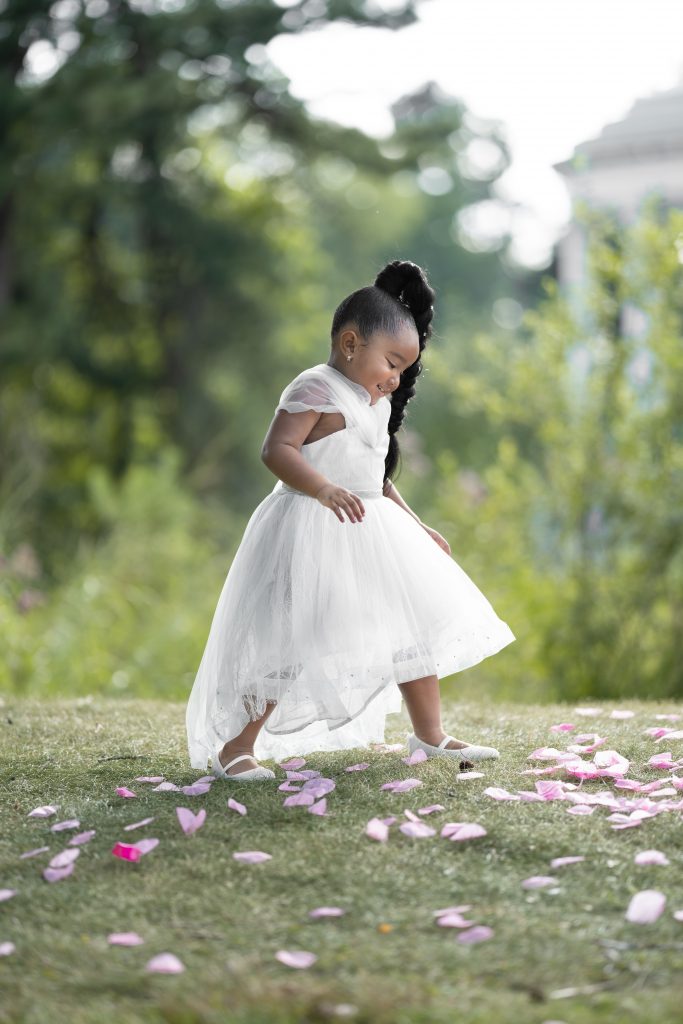 black flower girl walking through grass and rose petals
