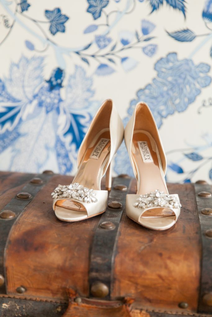 white badgley mischka shoes on a chest with blue wallpaper behind