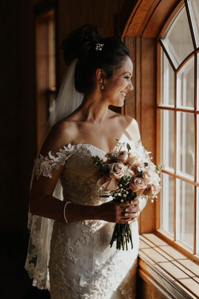 older bride looking out the window holding a bouquet