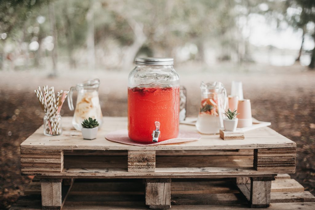 photo of a wooden pallet with pink lemonade and water pitchers on top in the woods for a fancy bar set up