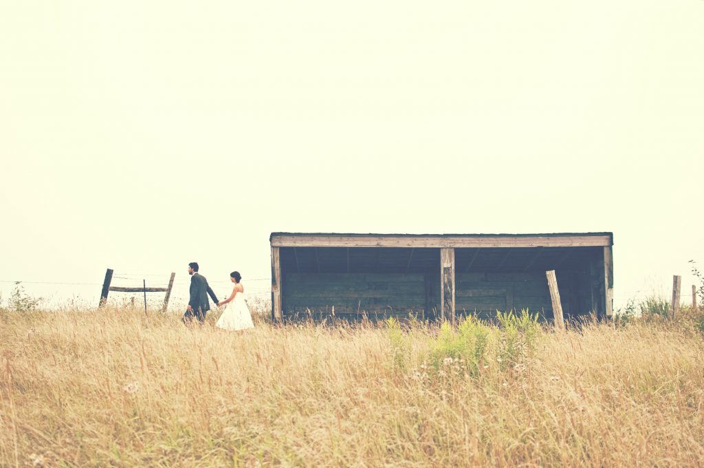 bride and groom walking in a field past an empty barn