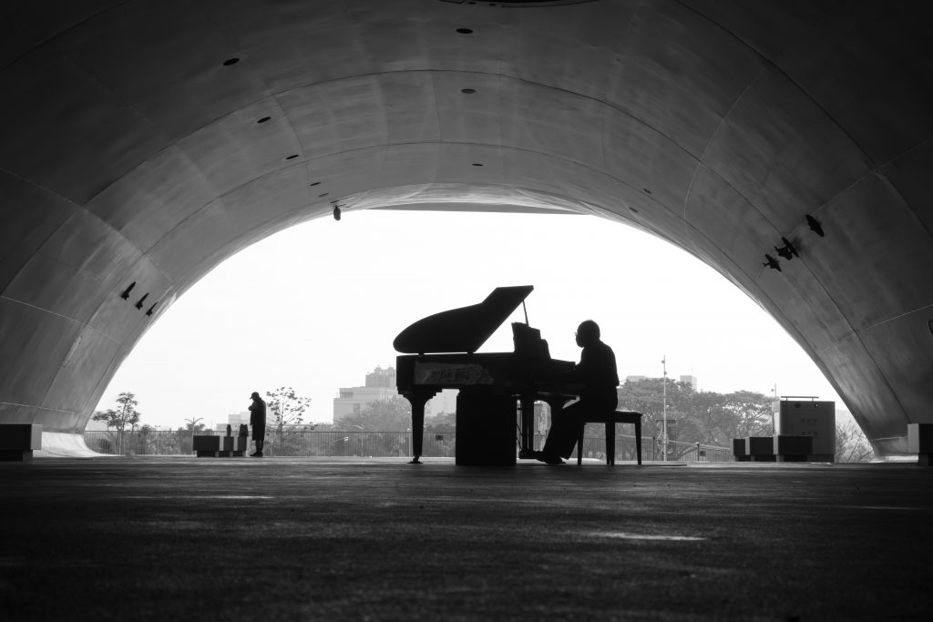 black and white photo of a man playing a grand piano outside