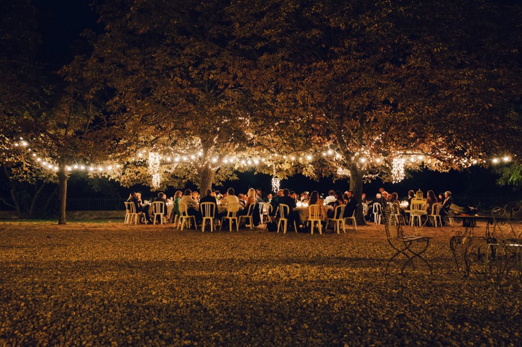 picture of an outdoor party at night under a tree with lots of string lights