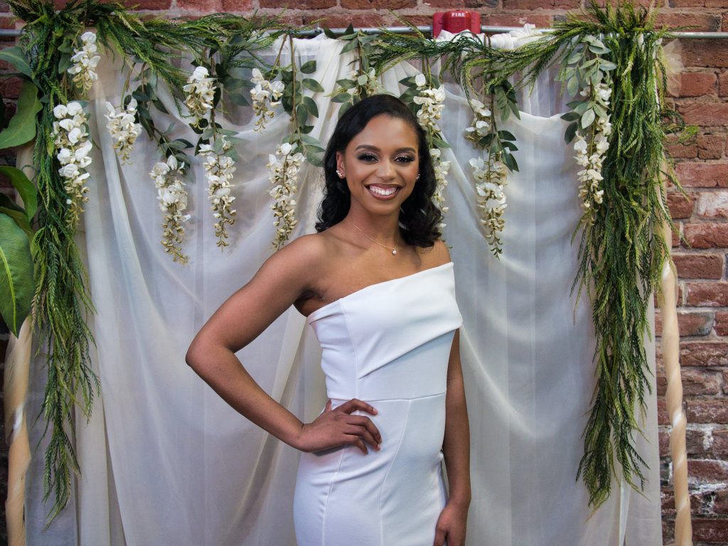 woman in white in front of a white and greenery backdrop for a bridal shower