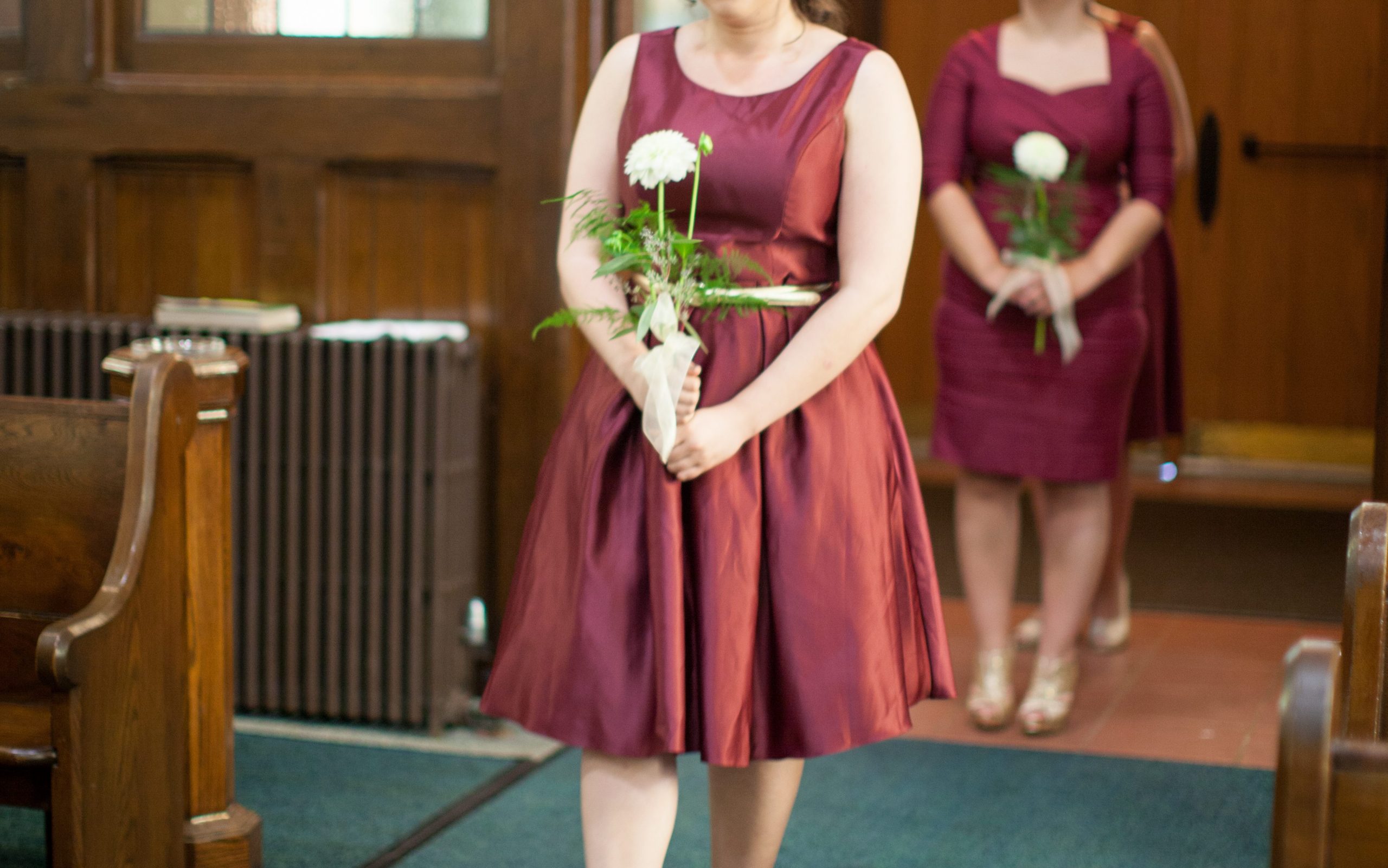 Bridesmaids in burgundy dresses holding a white statement flower