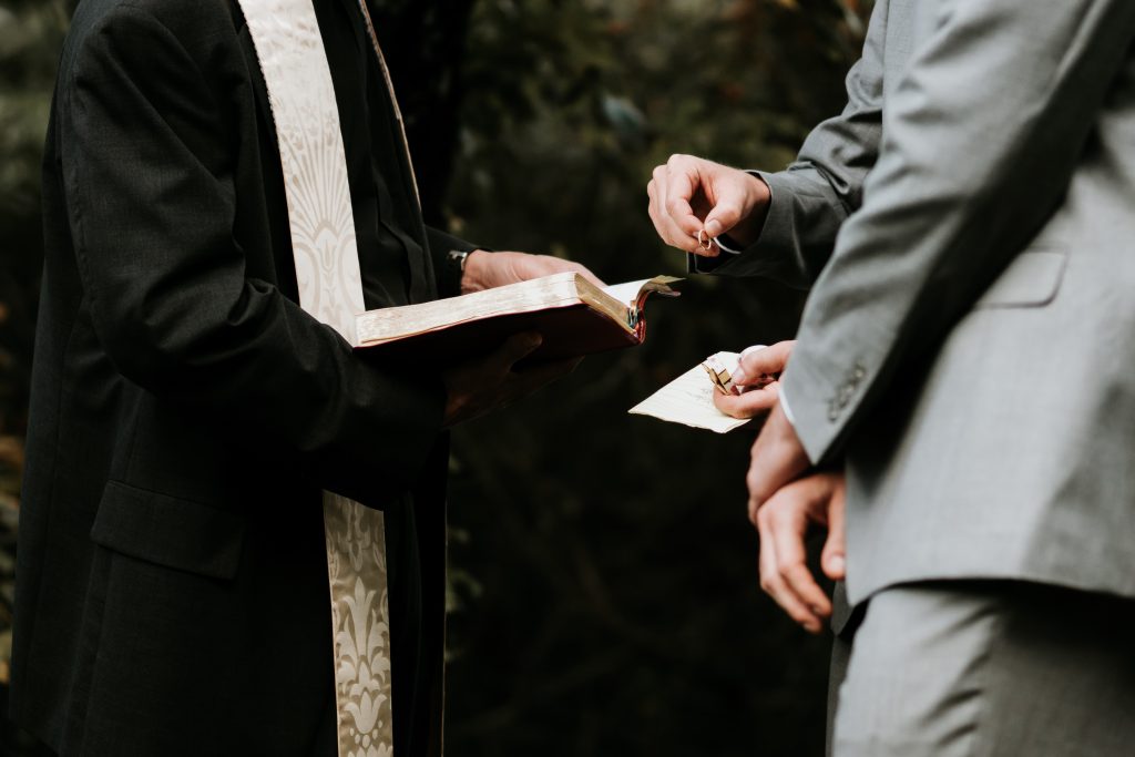 two grooms getting married by an officiant in a black robe with gold sash